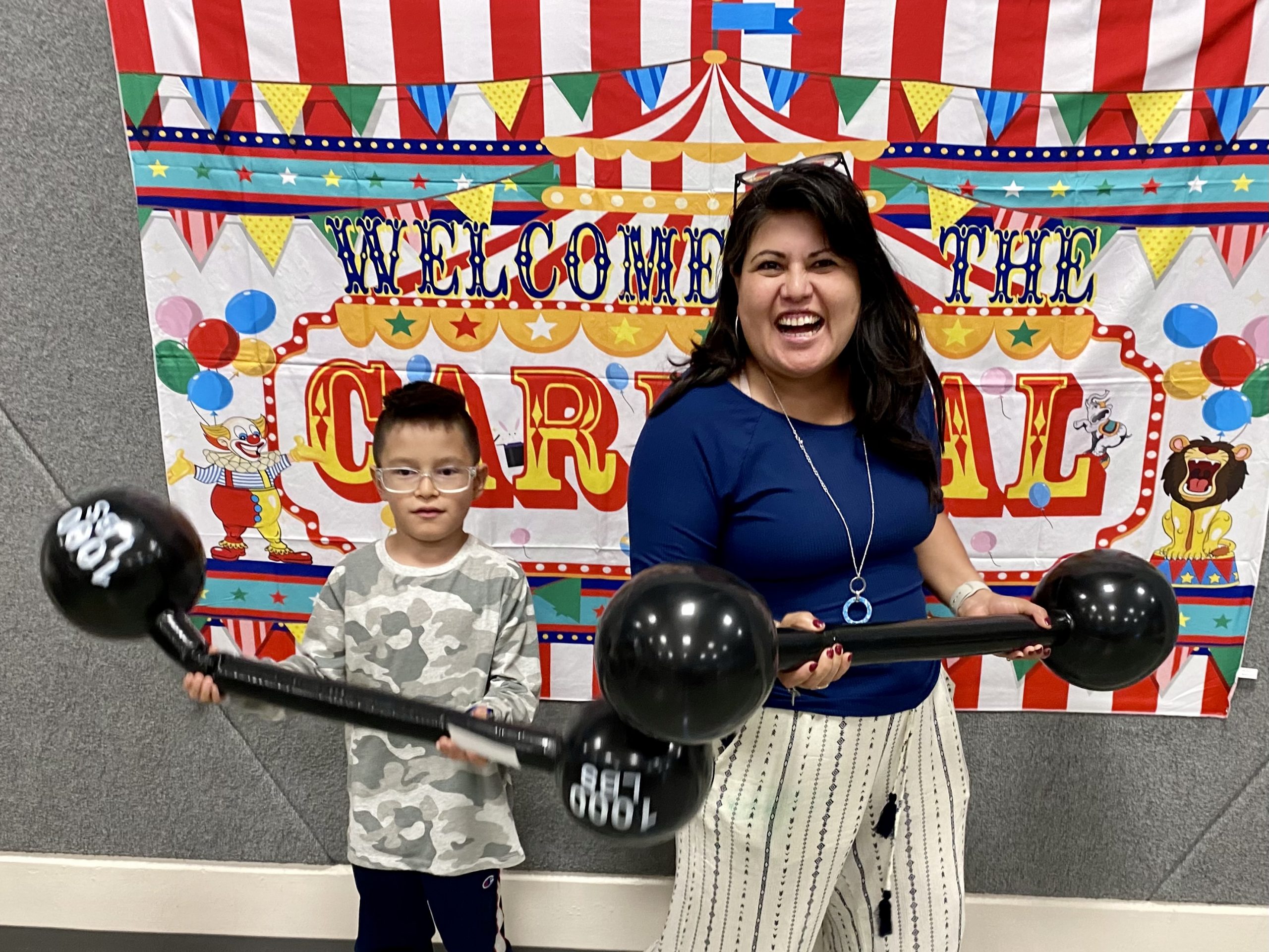 A mom and student holding barbell props at Literacy Night